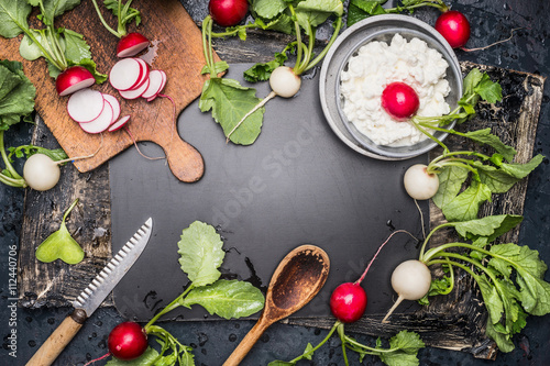 Food background with fresh radishes, kitchen tools and fresh cheese. Radishes salad making. Radishes and ingredients for salad on dark rustic background, top view, frame