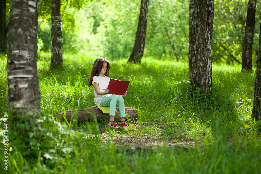 Charming little girl in forest with book sitting on tree stump Charming little girl in forest with book sitting on tree stump