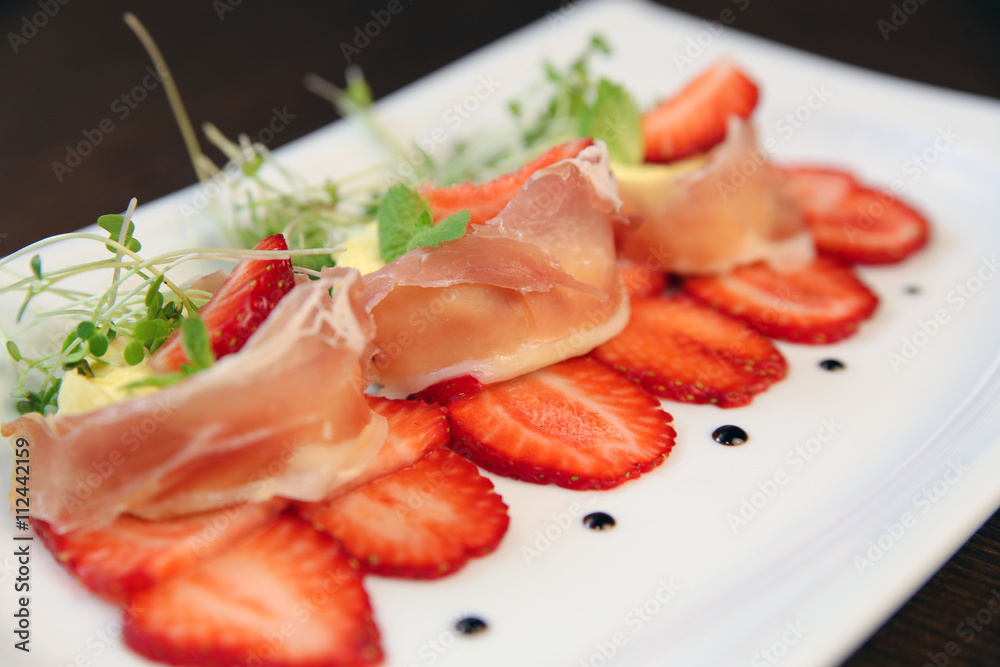 layered dessert with strawberries, biscuit cake and cream cheese on a dark wood background