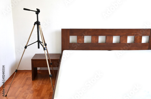 Tripod for camera next to the wooden bed in bedroom photo