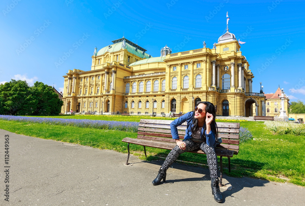 Attractive woman sitting on bench, enjoying sunny day in springtime in front of public Croatian national theater in Zagreb, capital of Croatia