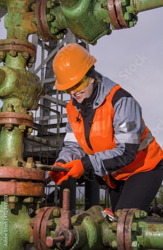 Woman engineer in the oil field repairing wellhead with the wrench wearing orange helmet and work clothes. Oil and gas concept. 