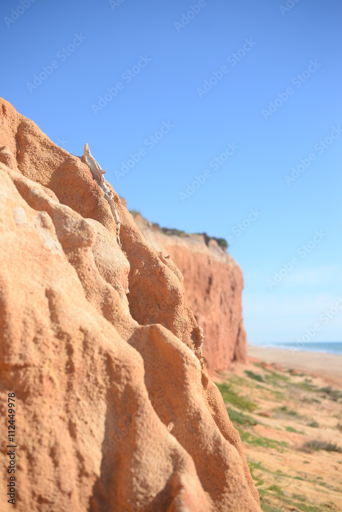 Red rock wall with defocused beach and ocean. Sunny outdoors background