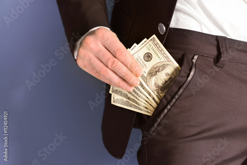 Man getting dollar banknotes out of suit pocket on grey background