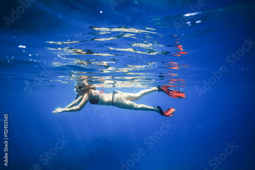 Fototapeta Naklejka Na Ścianę i Meble -  The girl floats on the surface of the ocean with snorkel and fins. Photo underwater