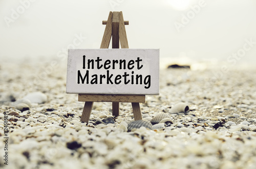 conceptual image with word INTERNET MARKETING on white canvas frame with wooden tripod stand.Blurred Clamshell and cockles background. photo