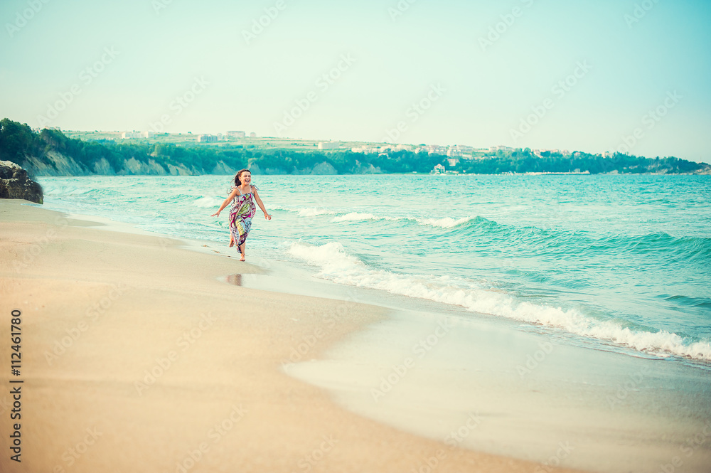 Child running along the seacoast. Girl in a colorful dress walking on the beach