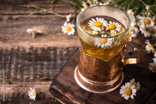 herbal chamomile tea on a wooden table. Chamomile tea in a transparent cup and camomile flowers on wooden table. Herbal tea for baby's stomach. Copy space.
