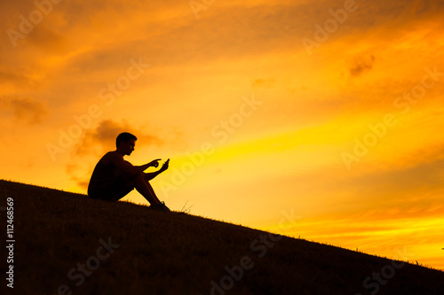 Silhouette of young man using his smart phone against a beautiful sunset. 