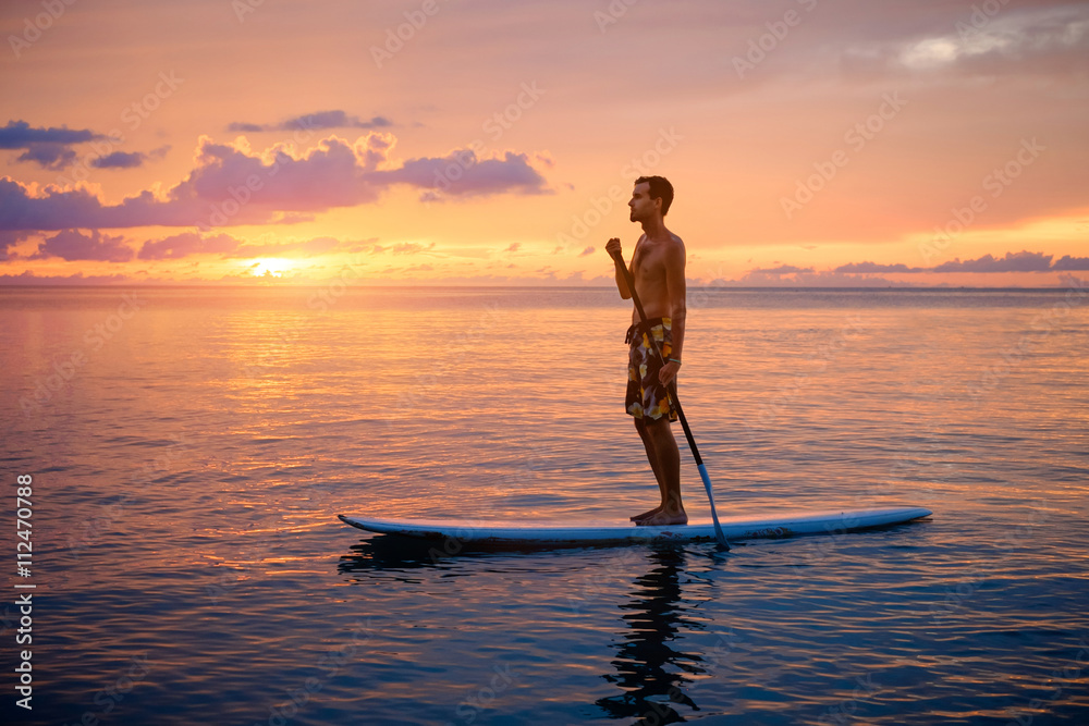 Silhouette of man paddleboarding at sunset