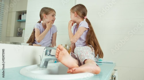 Girl looks at their teeth sitting near the mirror in the bathroom