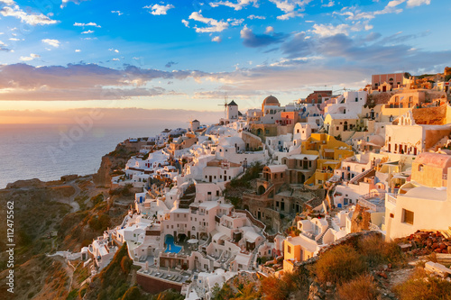 Picturesque view, Old Town of Oia or Ia on the island Santorini, white houses, windmills and church with blue domes at sunset, Greece © Kavalenkava