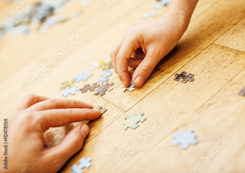 little kid playing with puzzles on wooden floor together with parent, lifestyle people concept, loving hands to each other