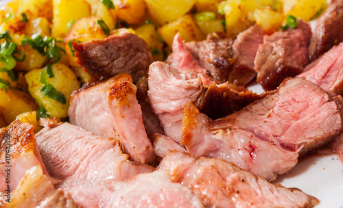 Sliced medium rare grilled Steak Ribeye with potato in a plate on wooden table