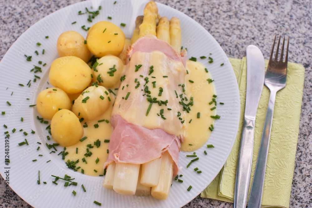 Boiled white asparagus with the ham and fresh new boiled potatoes served with the hollandaise sauce and small pieces of choped chives. Very healthy fresh seasonal dish typical for german cuisine. Boiled white asparagus with the ham and fresh new boiled potatoes served with the hollandaise sauce and small pieces of choped chives. Very healthy fresh seasonal dish typical for german cuisine.