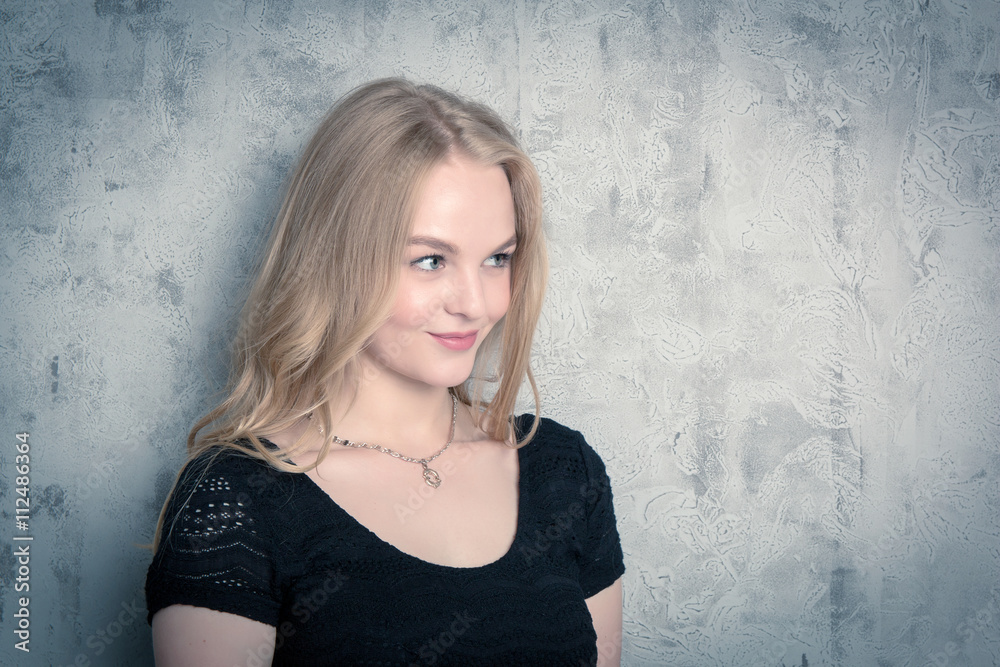 Fototapeta premium Attractive girl posing in a black evening dress. Toned portrait of blonde woman in studio