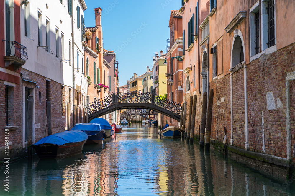 Venice canal with bridge and old brick buildings. Anchored boats in Venice canals with bridge clear sky and colorful buildings.