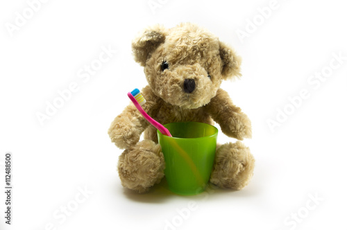 Teddy bear with a toothbrush in green plastic glasson white background