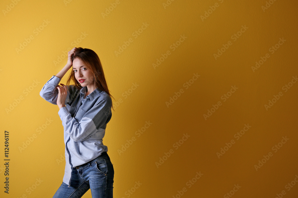 Beautiful young woman in shirt and jeans on yellow wall background Beautiful young woman in shirt and jeans on yellow wall background