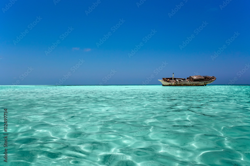 clear ocean maldives water under blue sky with abandoned boat