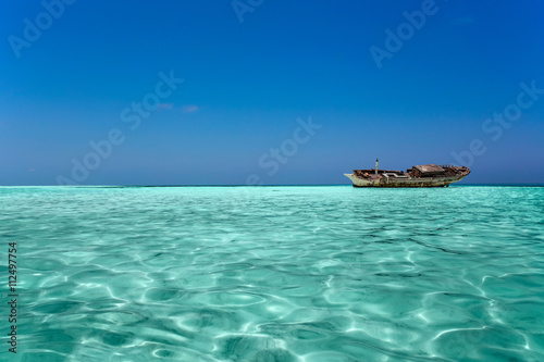 clear ocean maldives water under blue sky with abandoned boat