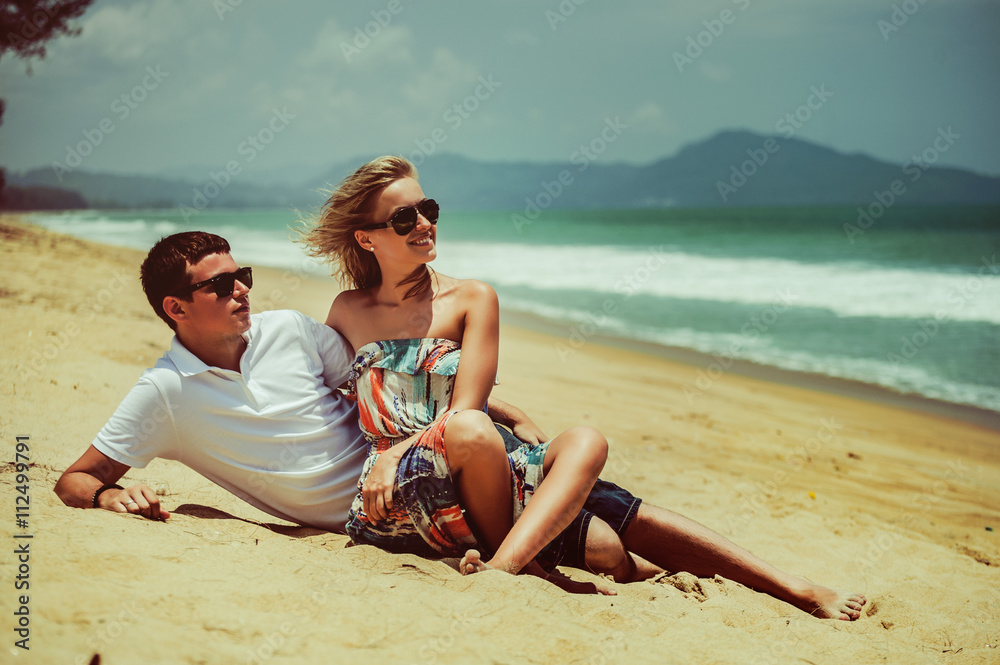 Happy couple in sunglasses lying on background of sandy beach and watching the sea