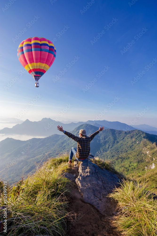 Obraz premium man on top of mountain. Phu cheefa park Chiangrai Thailand. Colorful hot-air balloon flying over the mountain.