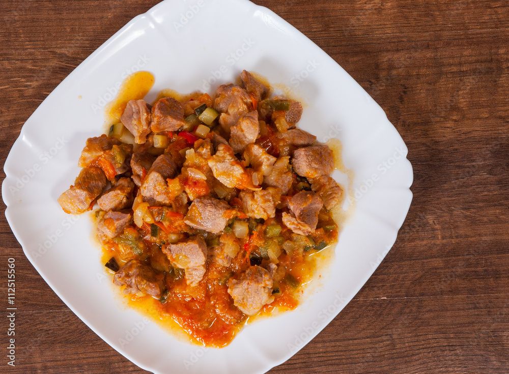 Stewed meat with vegetables in a plate on wooden table