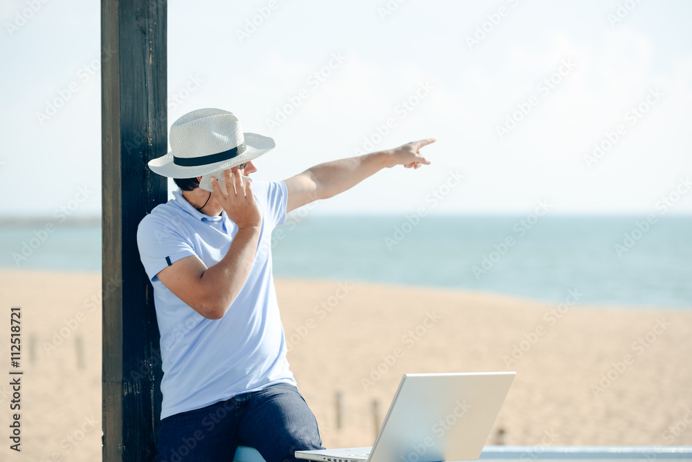Businessman pointing outside and working with laptop, talking on phone.