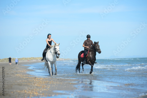 happy young couple vacation riding horses on the beach in a sunny summer day