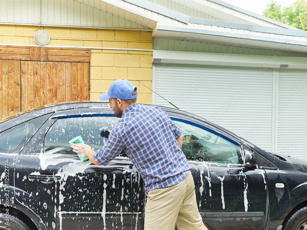 Man washing his black car near house.