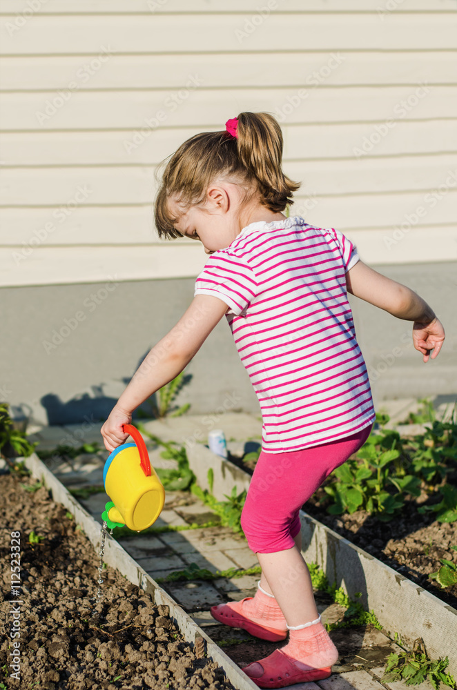 Fototapeta premium little girl watering plants from a watering can