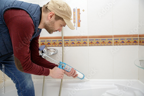 Plumber caulking bathtub with silicone glue using caulking gun.