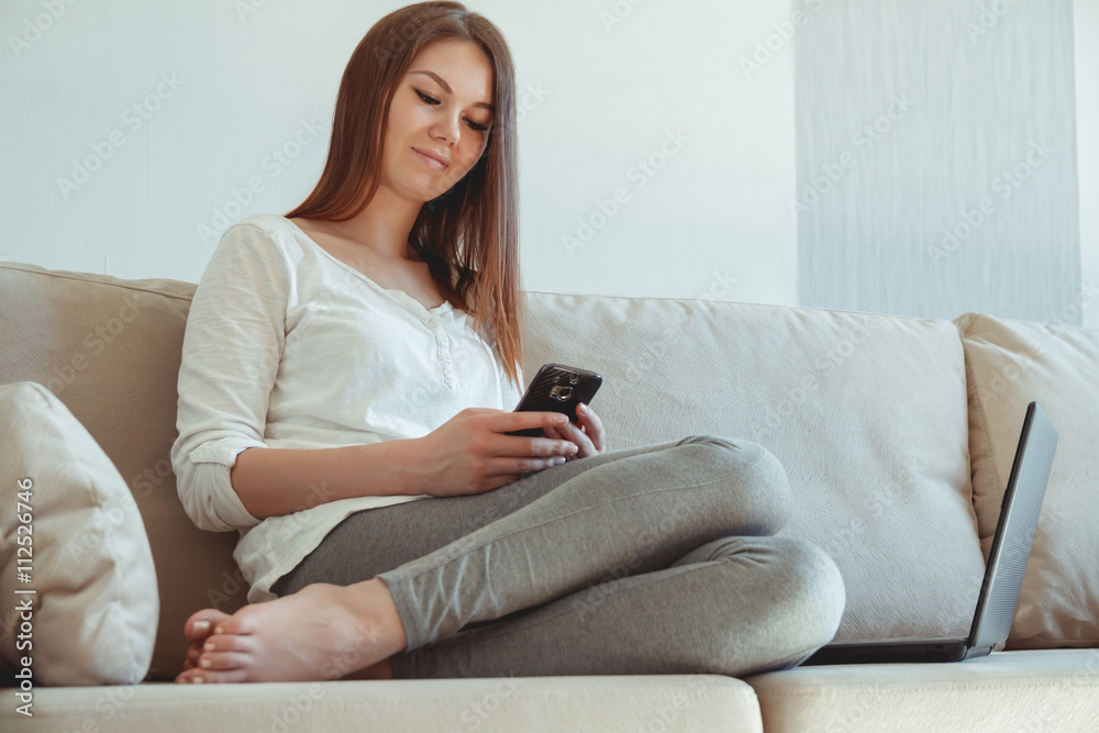 Young girl sitting on the couch with a laptop and mobile phone. Work at home concept Young girl sitting on the couch with a laptop and mobile phone. Work at home concept