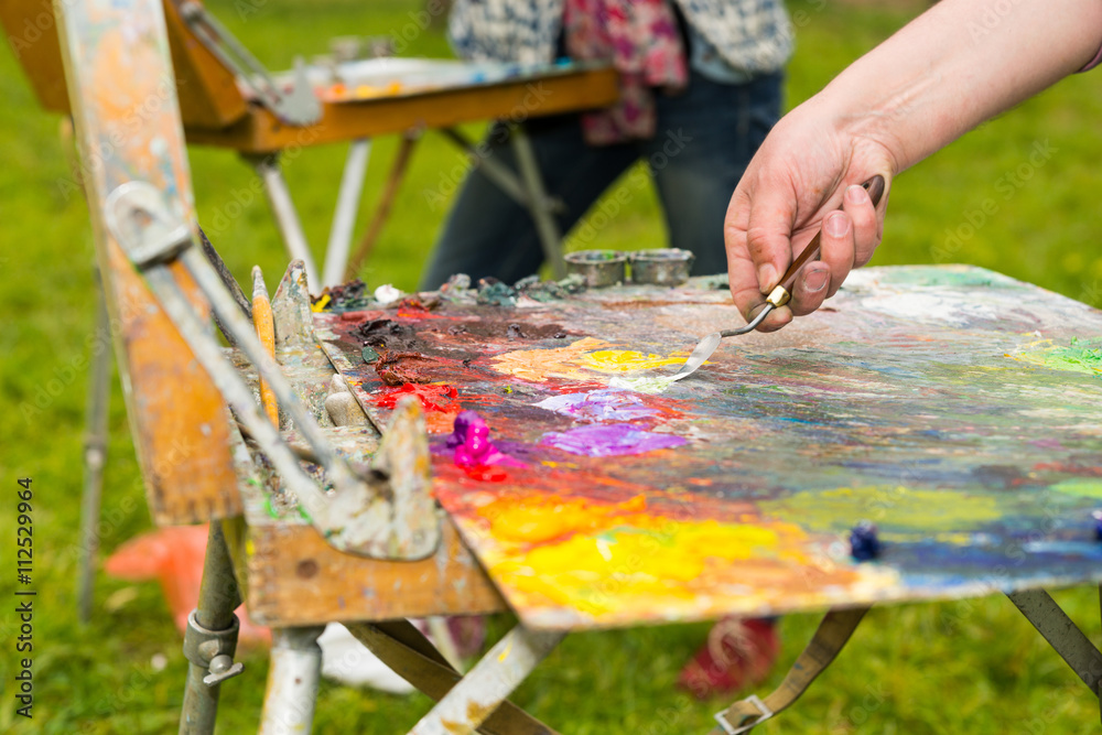 Male hand mixing oil paint on an old multiclored palette Male hand mixing oil paint on an old multiclored palette