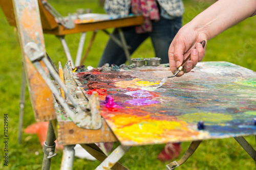 Male hand mixing oil paint on an old multiclored palette