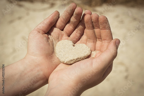People heart concept. Child's hands holding heart made of sand.