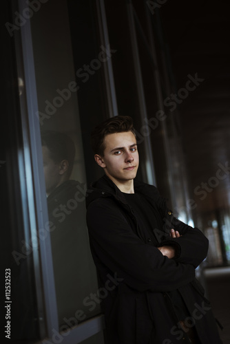 Young handsome man in black coat standing near shop with hands c