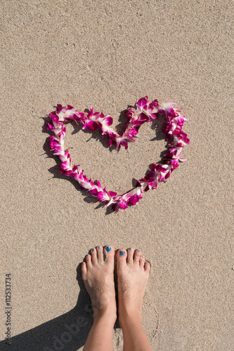 orchid flower garland necklace in love heart shape with woman feet on white sand beach romantic couple honeymoon trip at Hawaii  
