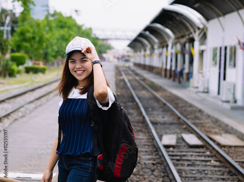 young asian girl waiting for the train in station waiting train with smile and happy moment  single alone woman at train station with back pack for travel  filter effect
