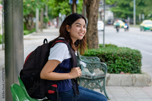 Young woman standing at bus stop on street city. Asian woman waiting for bus. Woman student in private dress standing at bus stop. Public transport stop in Thailand. bus stop on street in asian.