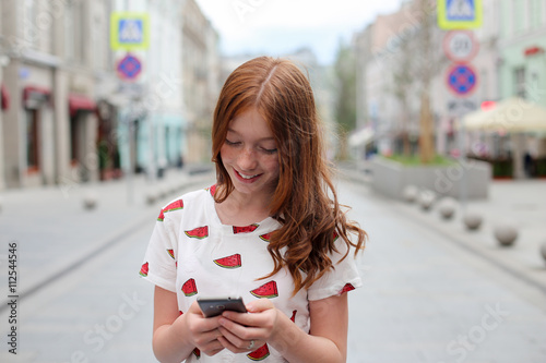 Front view of a fashion happy girl walking and using a smart phone on a city street