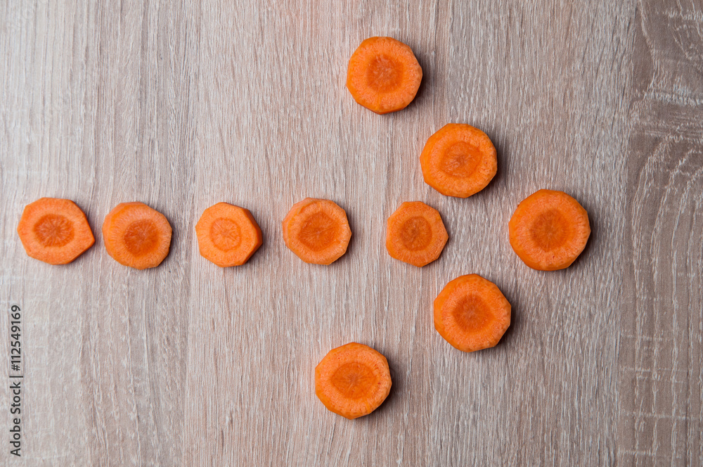 Pieces of carrots on a wooden table arranged in the shape of an Pieces of carrots on a wooden table arranged in the shape of an