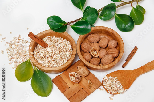 There are with Walnuts and Rolled Oats in the Wooden Plates with Sticks of Cinnamon,Wooden Support,Spoon,Green Leaves,Healthy Fresh Organic Food on the White Background,Top View photo