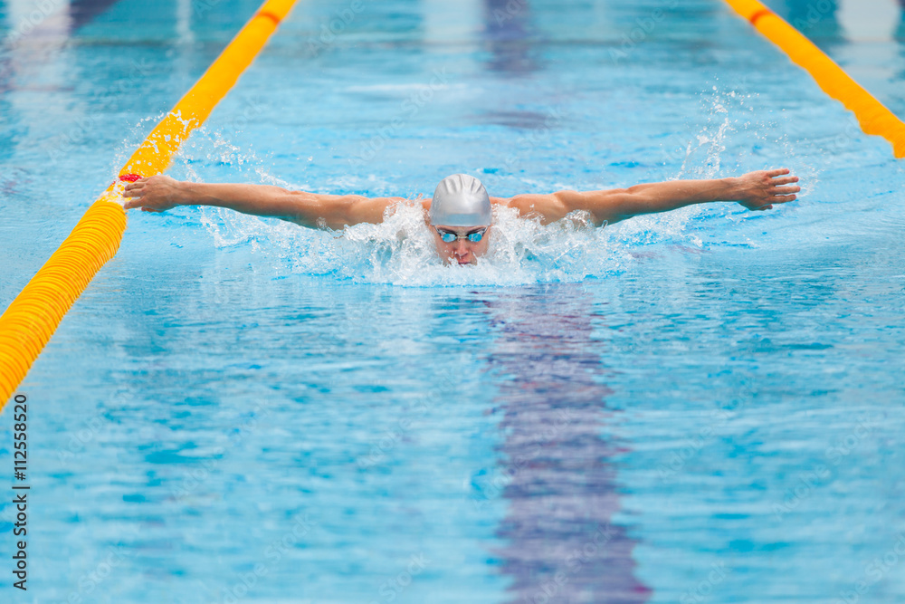 dynamic and fit swimmer in cap breathing performing the butterfly stroke