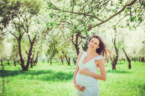 Pregnant woman in the apple orchard is holding tummy