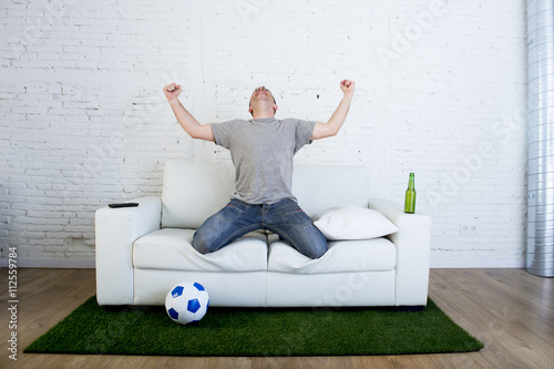 Fotografía football fan watching tv match on sofa with grass pitch carpet celebrating goal