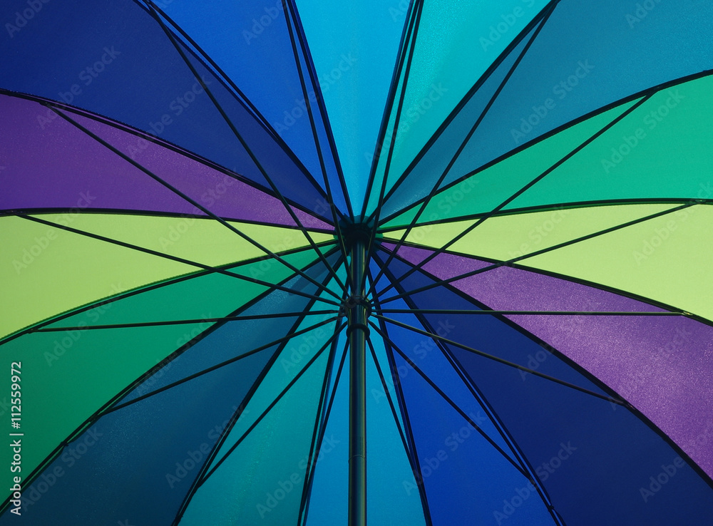 Detail of a colorful opened umbrella watched from underneath while sunshine


