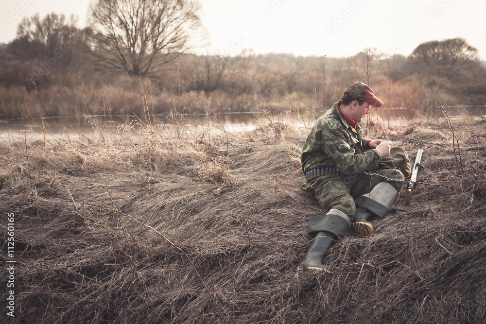 Hunter preparing for hunting in morinig field nearby river during sunrise