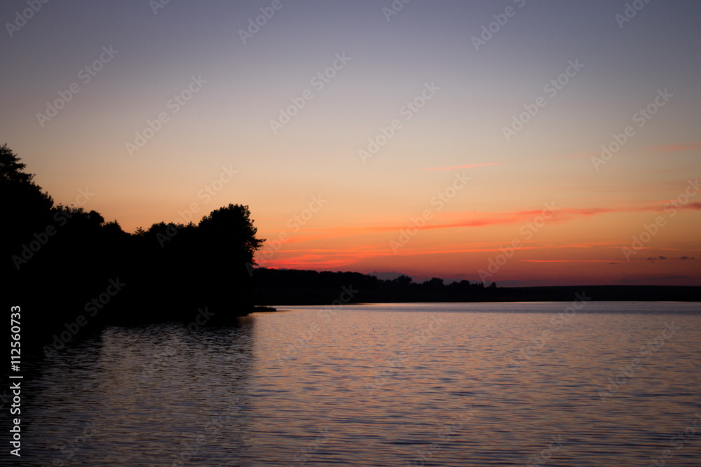 A beautiful sunset over the trees on the shore of the lake